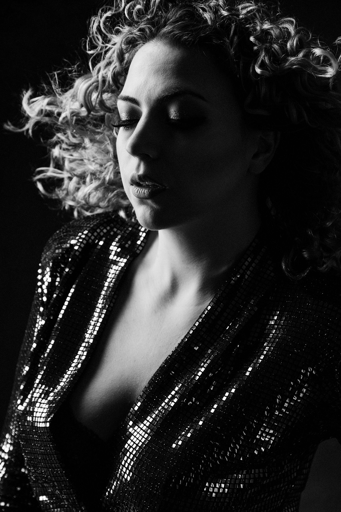 Dramatic black and white portrait with sequined jacket and curly hair in profile.