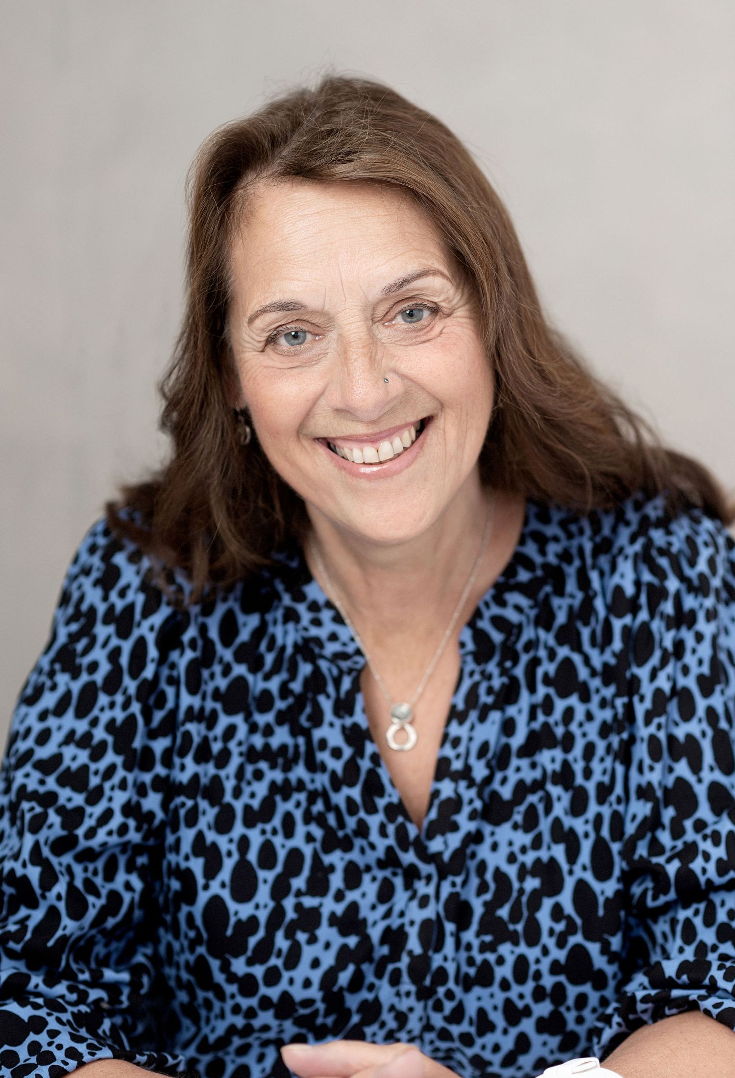 Professional headshot of person in blue leopard print top against neutral backdrop.