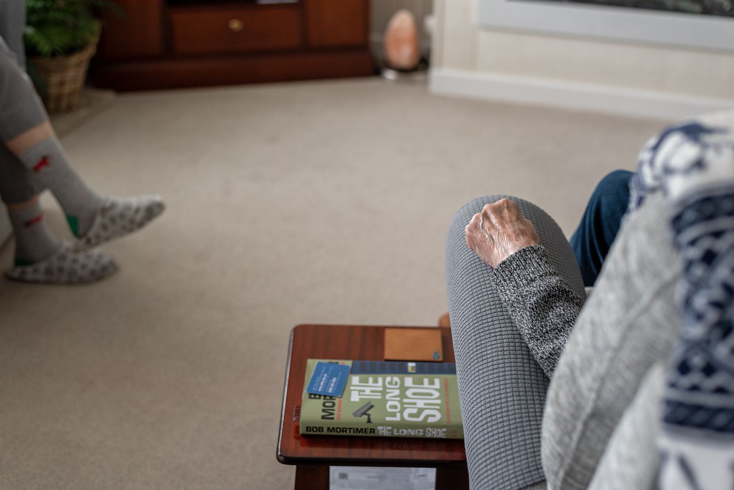 Person relaxing in a cozy living room with feet up on a wooden side table, holding a book, wearing gray leggings and a knit sweater.
