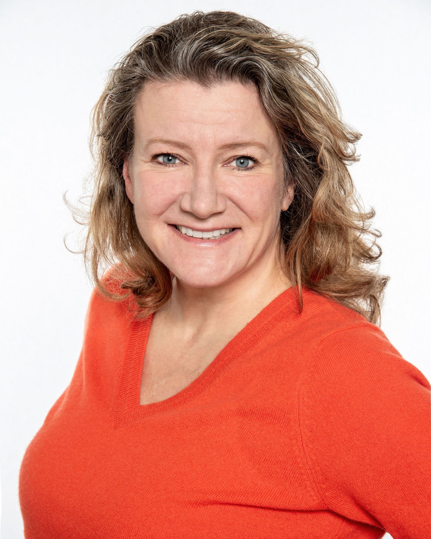 Professional portrait against white background featuring person in bright orange sweater.