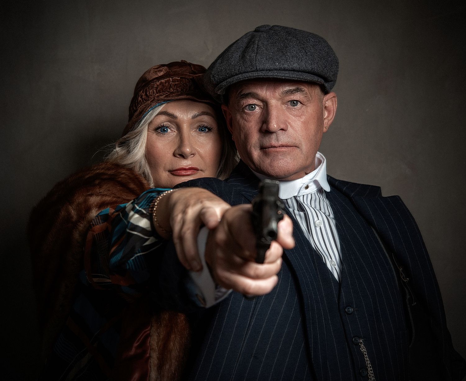 Dramatic noir-style portrait of couple in vintage clothing with one holding a gun.