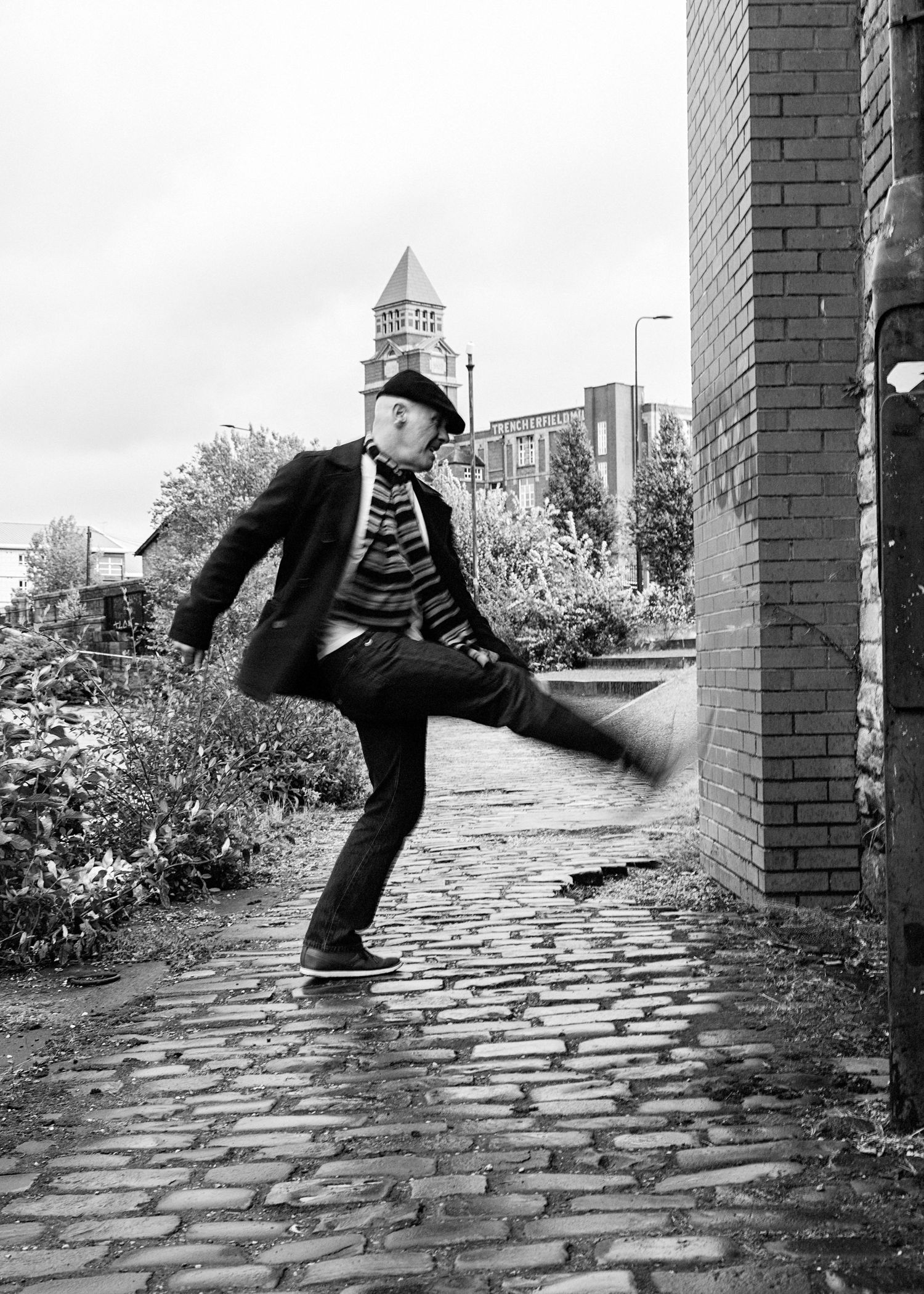 A black and white sequence of four images showing someone performing a parkour jump on a cobblestone path.