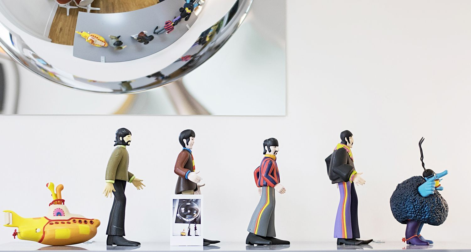 A collection of small figurines arranged in a horizontal line showing various Beatles characters and objects.