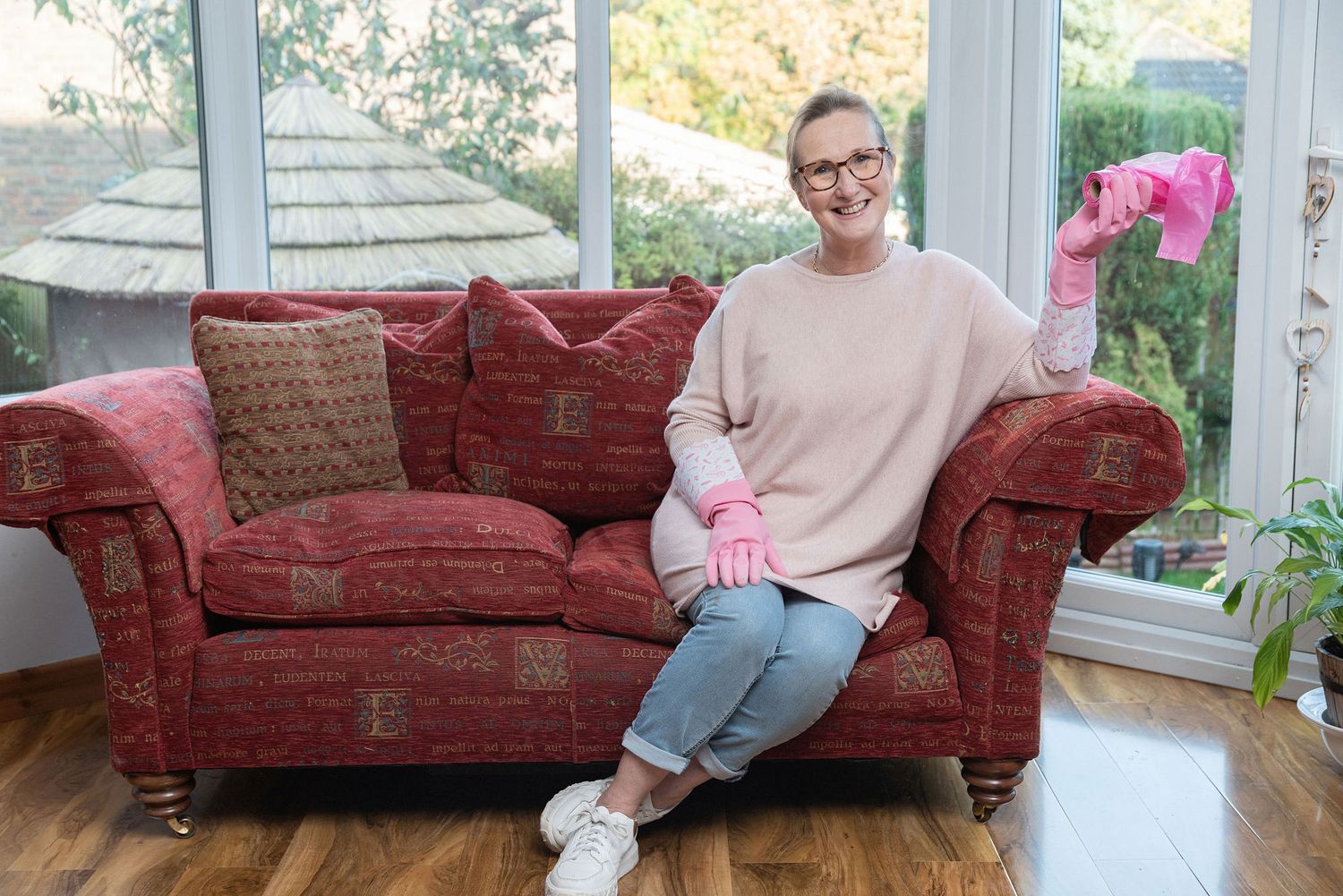 Person relaxing on a red floral couch in a bright sunroom.