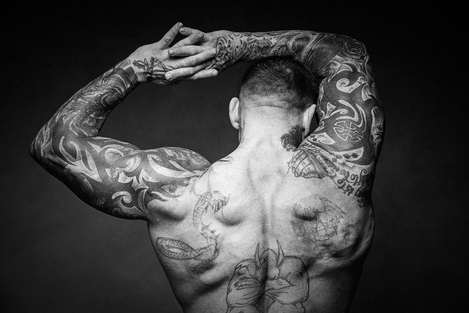 Black and white artistic photo showing tattooed back muscles and arms in dramatic lighting.