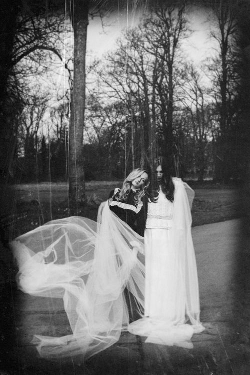 Black and white photo of two women outdoors with flowing white tulle fabric billowing around them.