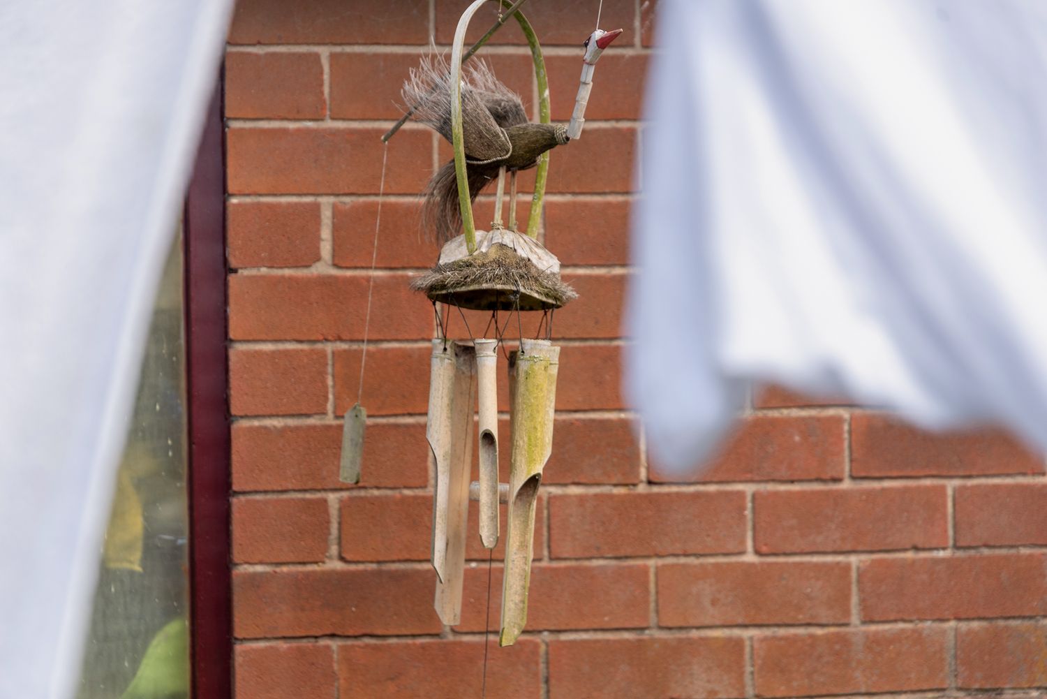 Rustic bamboo wind chime hanging against a red brick wall outdoors.