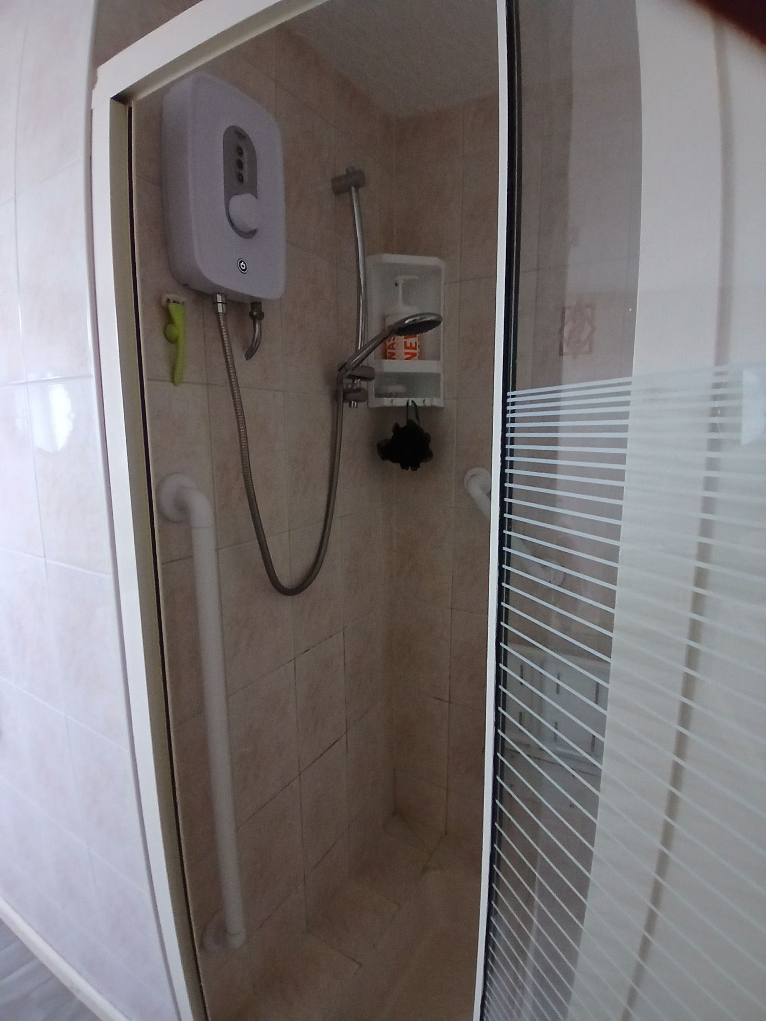 Interior view of a modern bathroom shower stall with glass door, white electric shower unit and beige tiled walls.