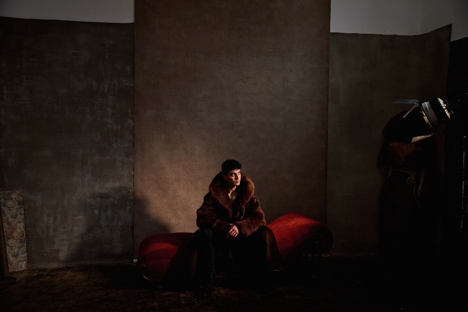 Moody low-light portrait of figure seated on red couch in dark room.