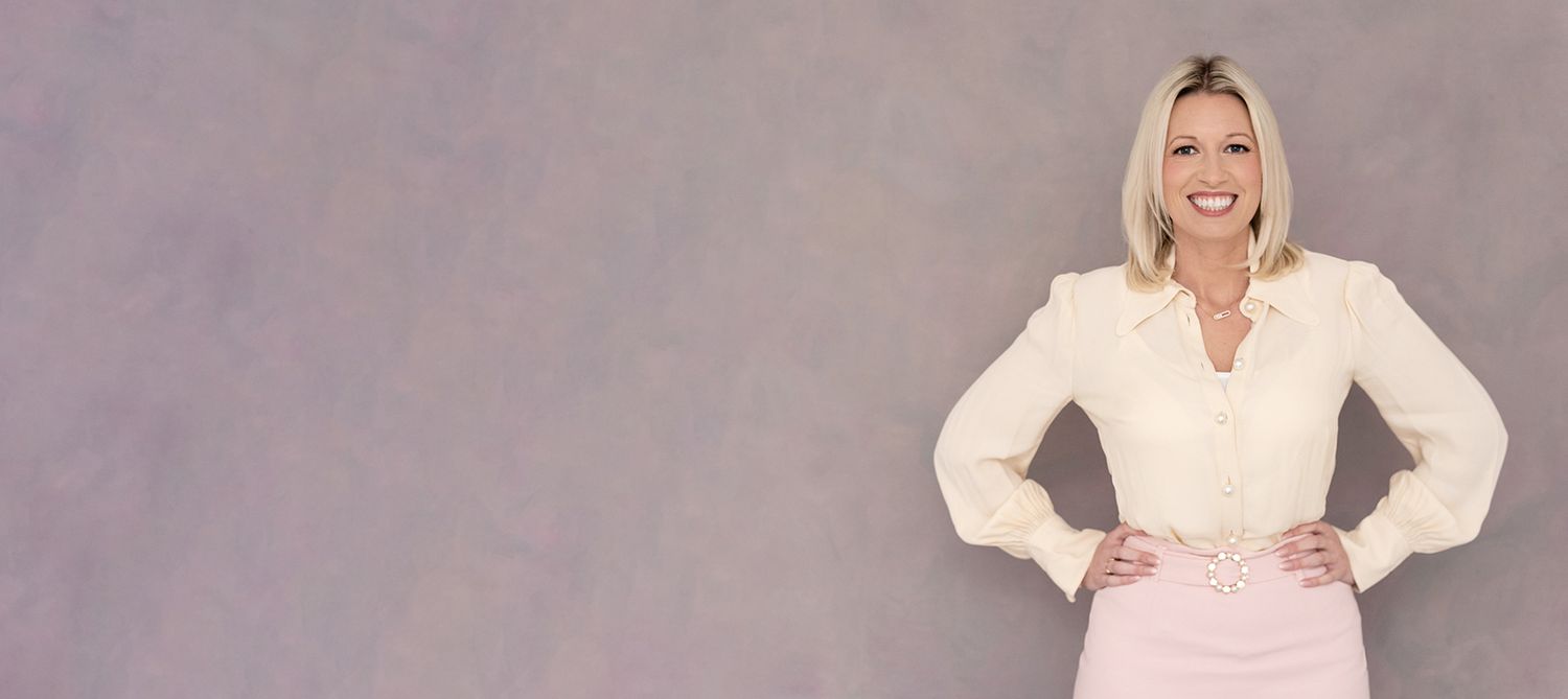 Professional portrait of person in white blouse and pink skirt against purple background.