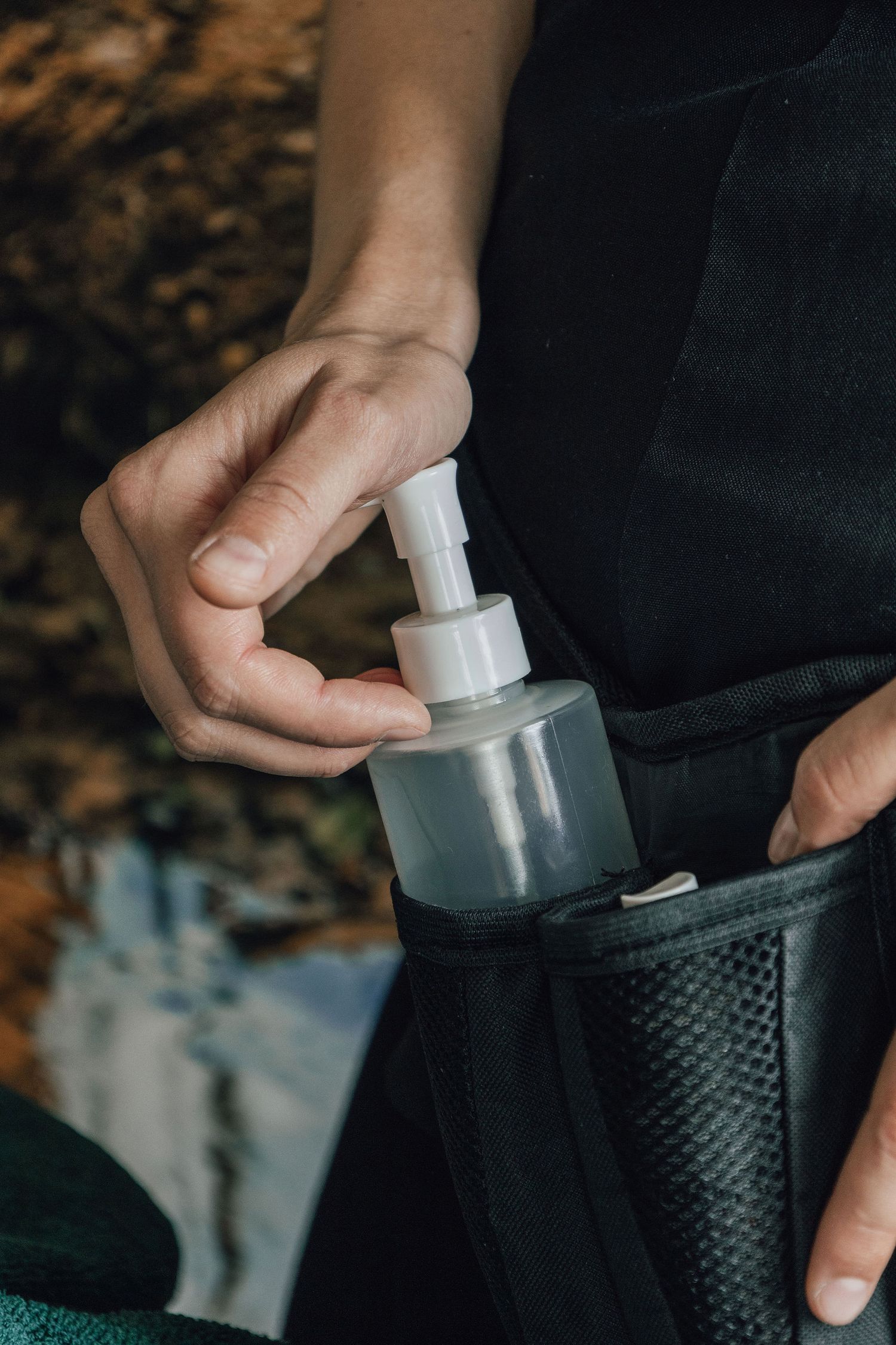 Hand holding massage oil or lotion dispenser bottle against dark background.
