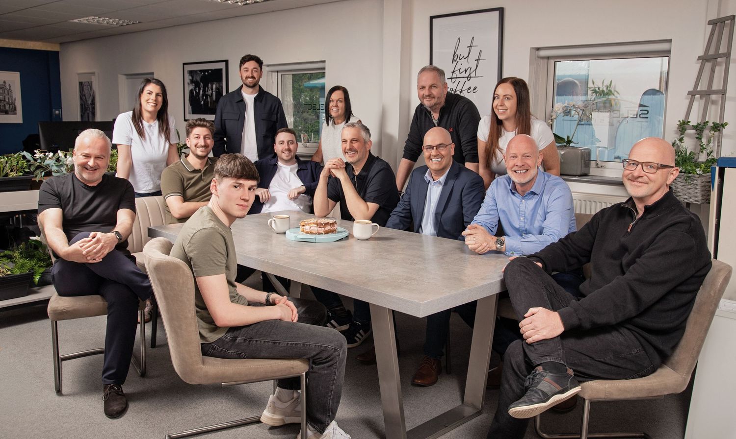 A diverse group of professionals smiling around a conference table in a modern office setting.
