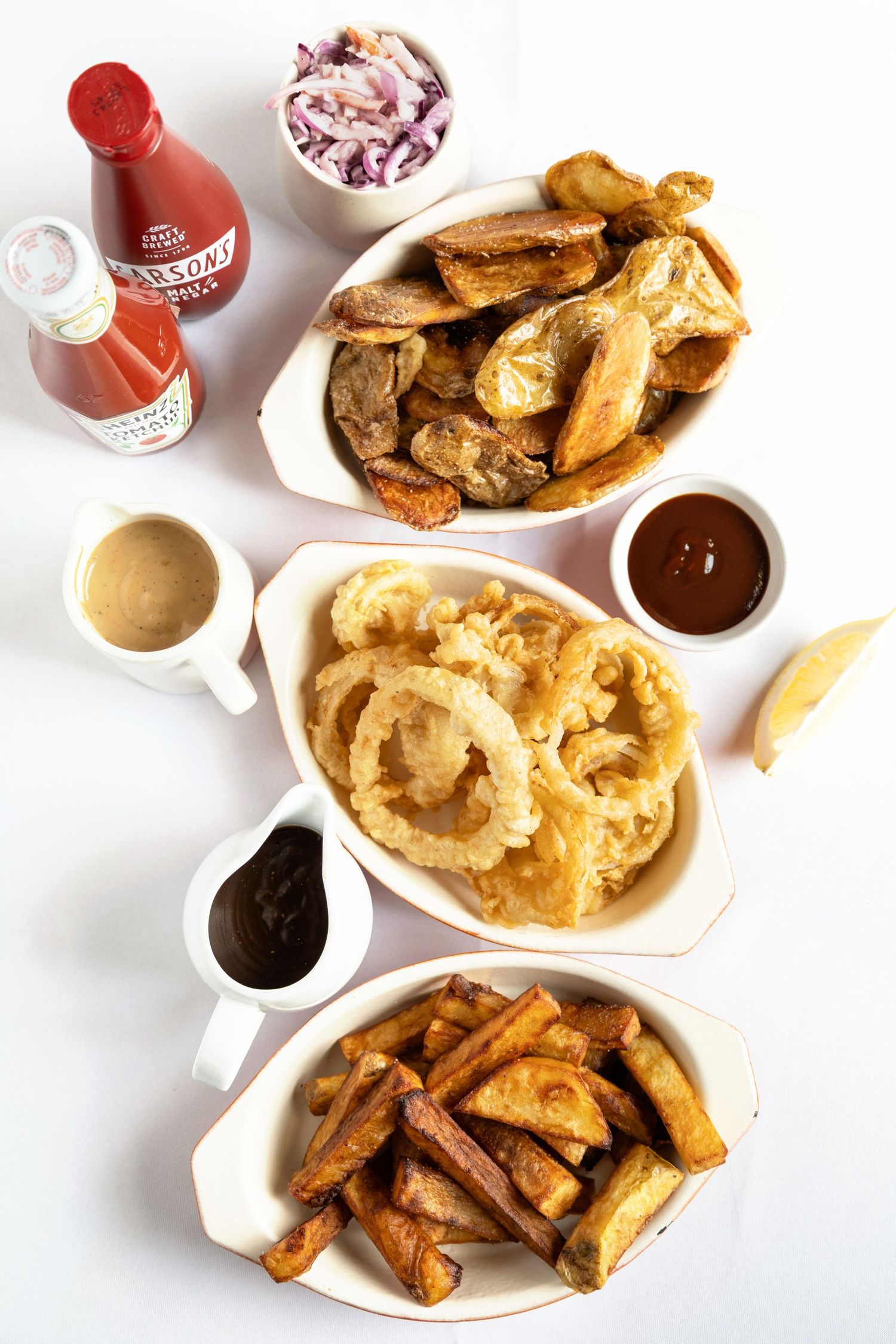 Overhead view of fried appetizers including onion rings, potato wedges, and chicken with dipping sauces and ketchup.