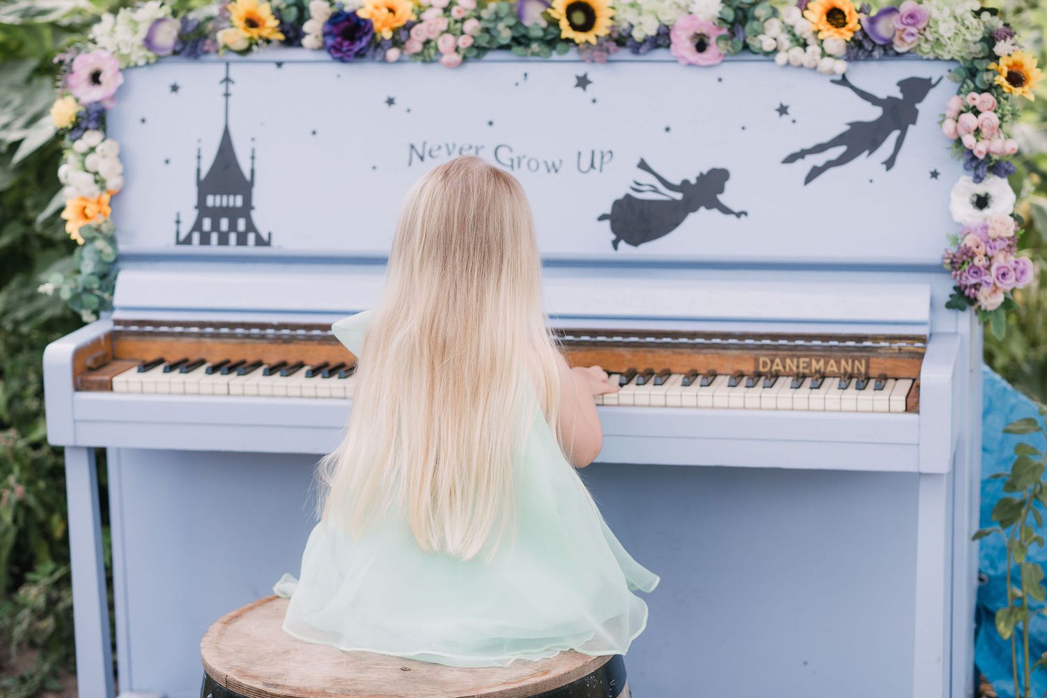 A mint-colored piano decorated with whimsical fairy tale designs shows a musical scene with flowers, castles and shadows.