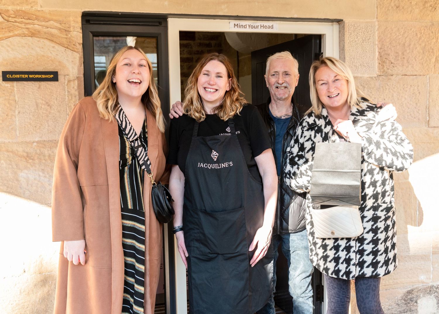 Small business team posing together in front of a storefront wearing casual attire.