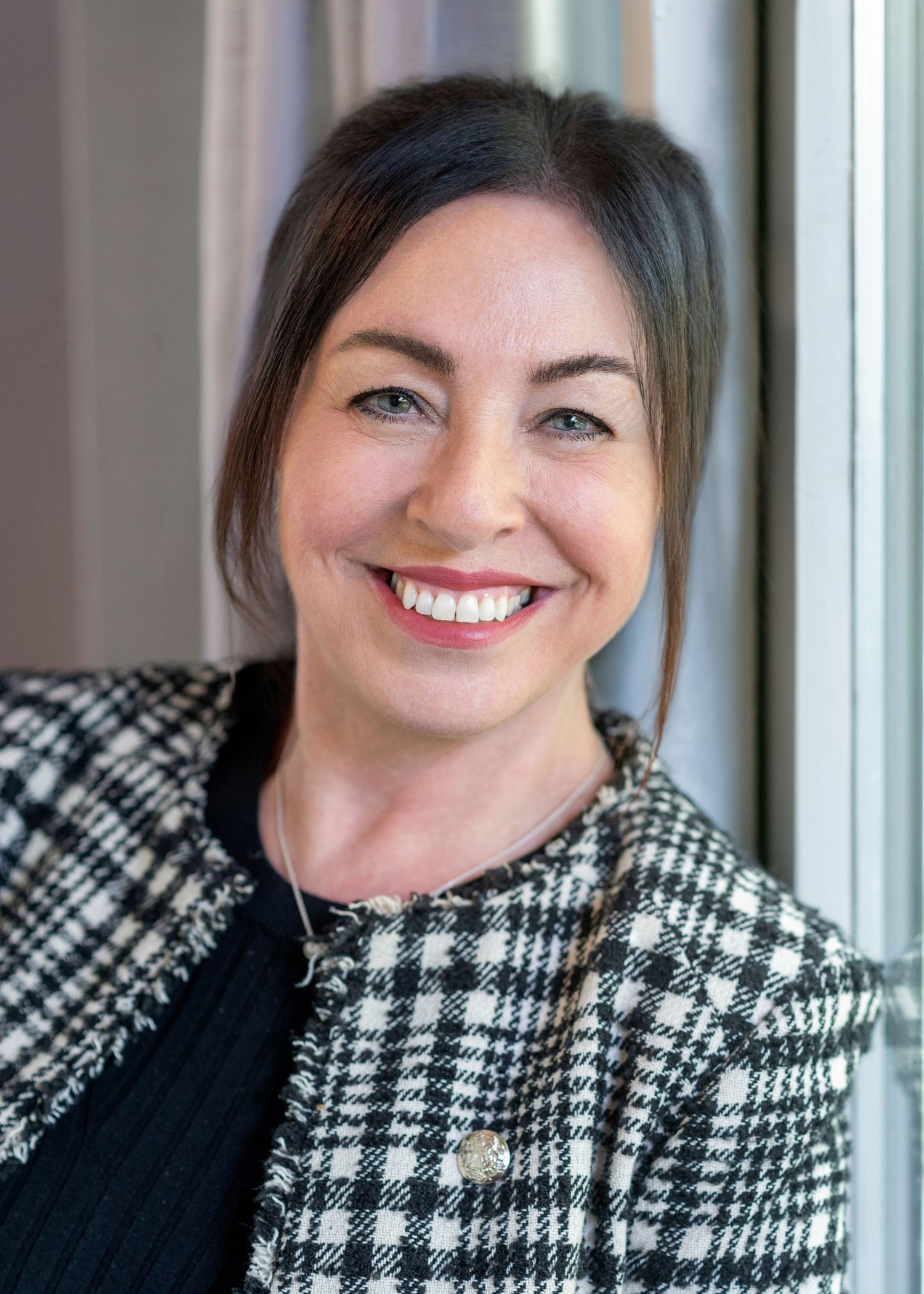 Professional portrait of a woman wearing a checkered jacket and dark top smiling warmly.