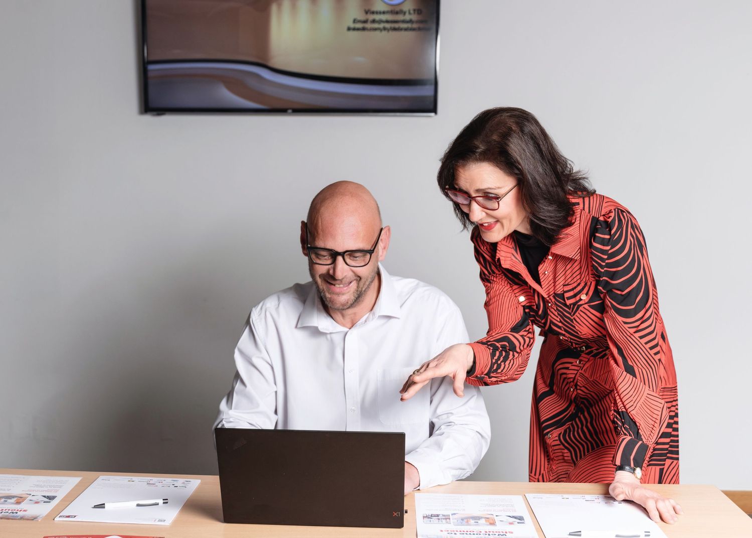 Two business colleagues smile while collaborating together at a laptop in an office environment.