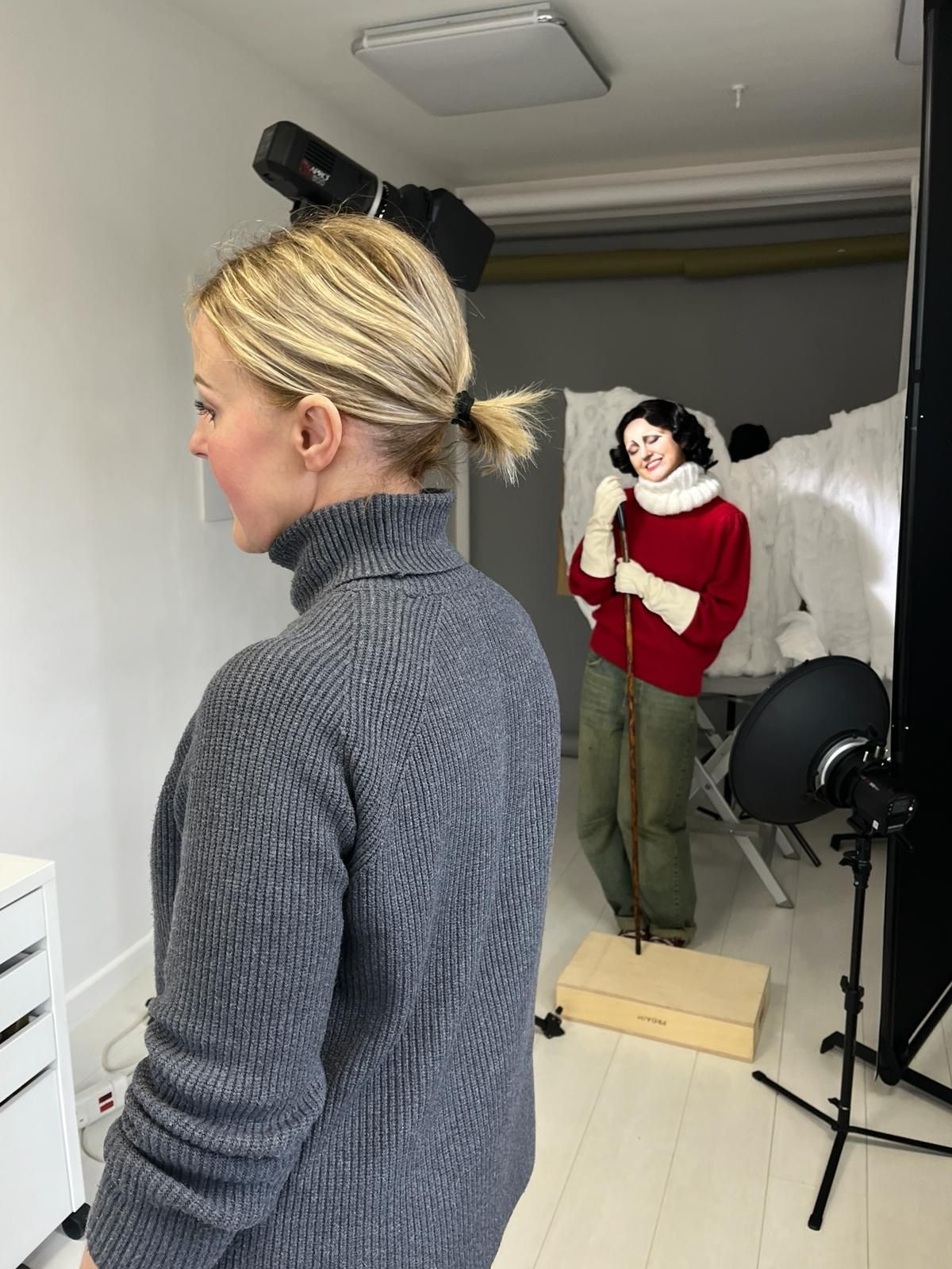 Side view of photographer working in studio with lighting equipment and backdrop visible.