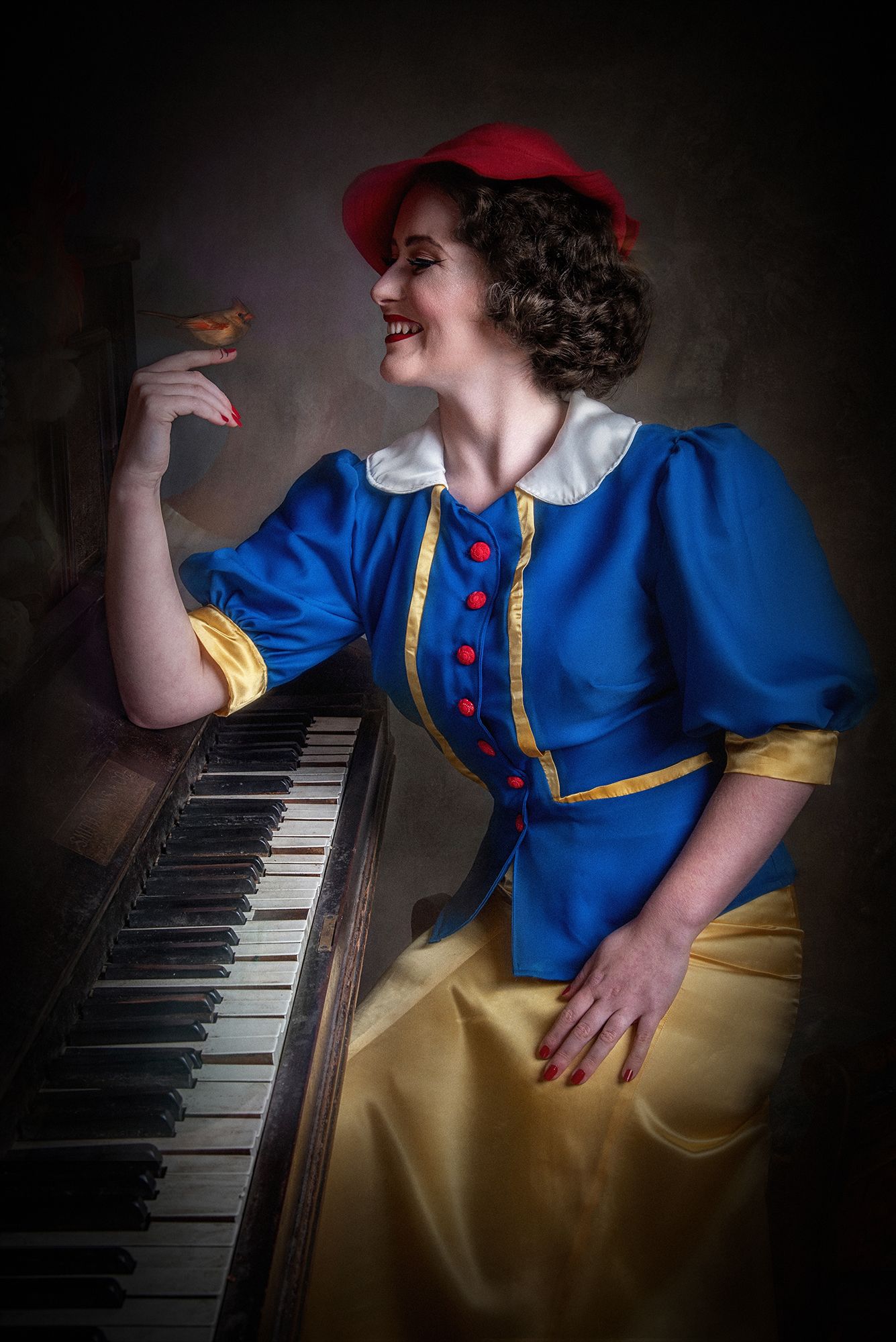 Fairytale-inspired portrait with bird perched on hand at piano in blue and yellow costume.