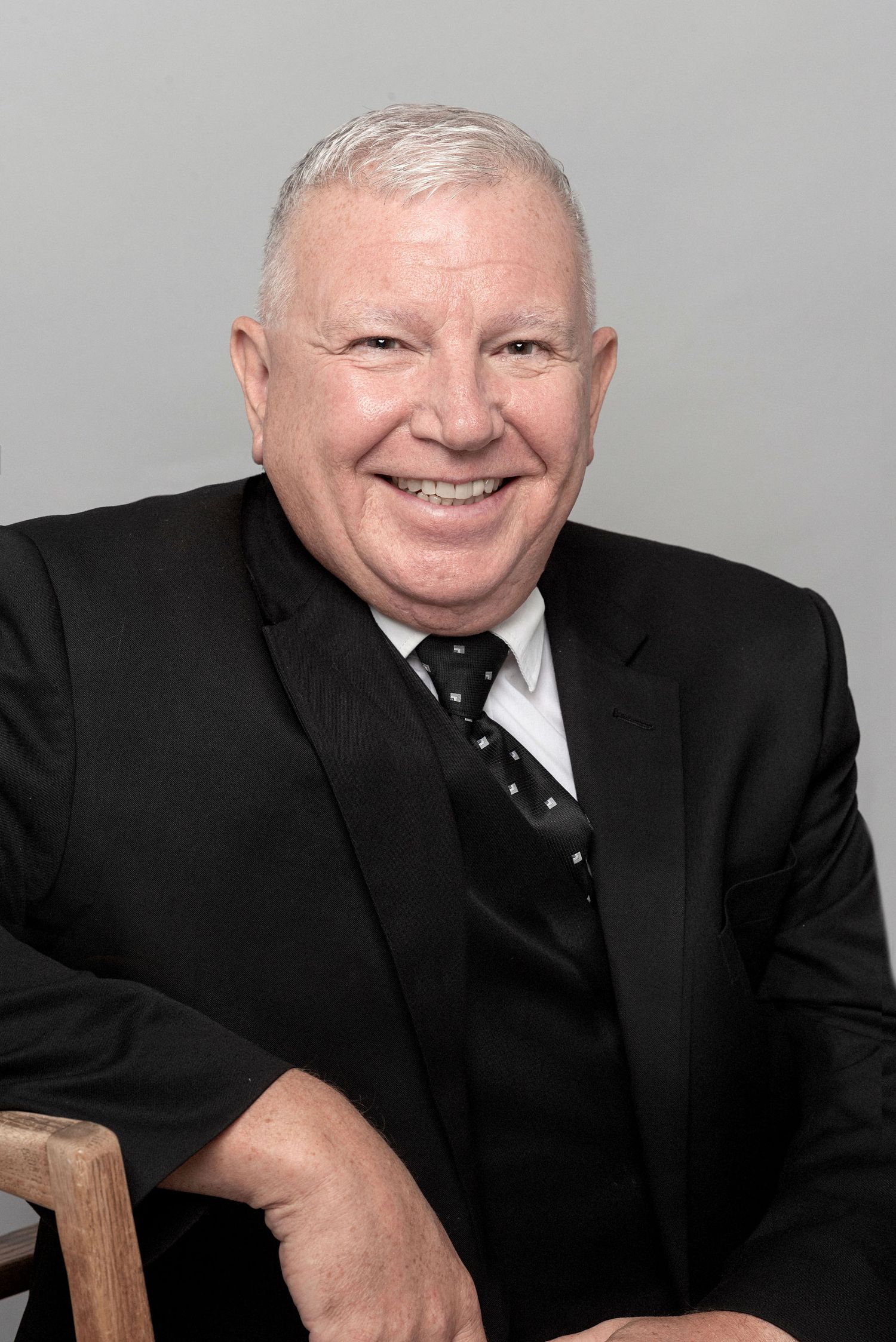 Business portrait of someone in a dark suit seated against a grey background.