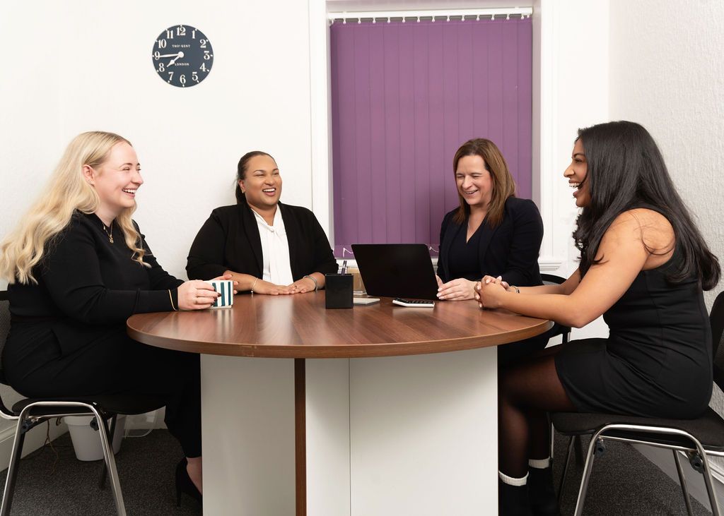 Group of coworkers having a casual conversation around a circular table in an office setting.