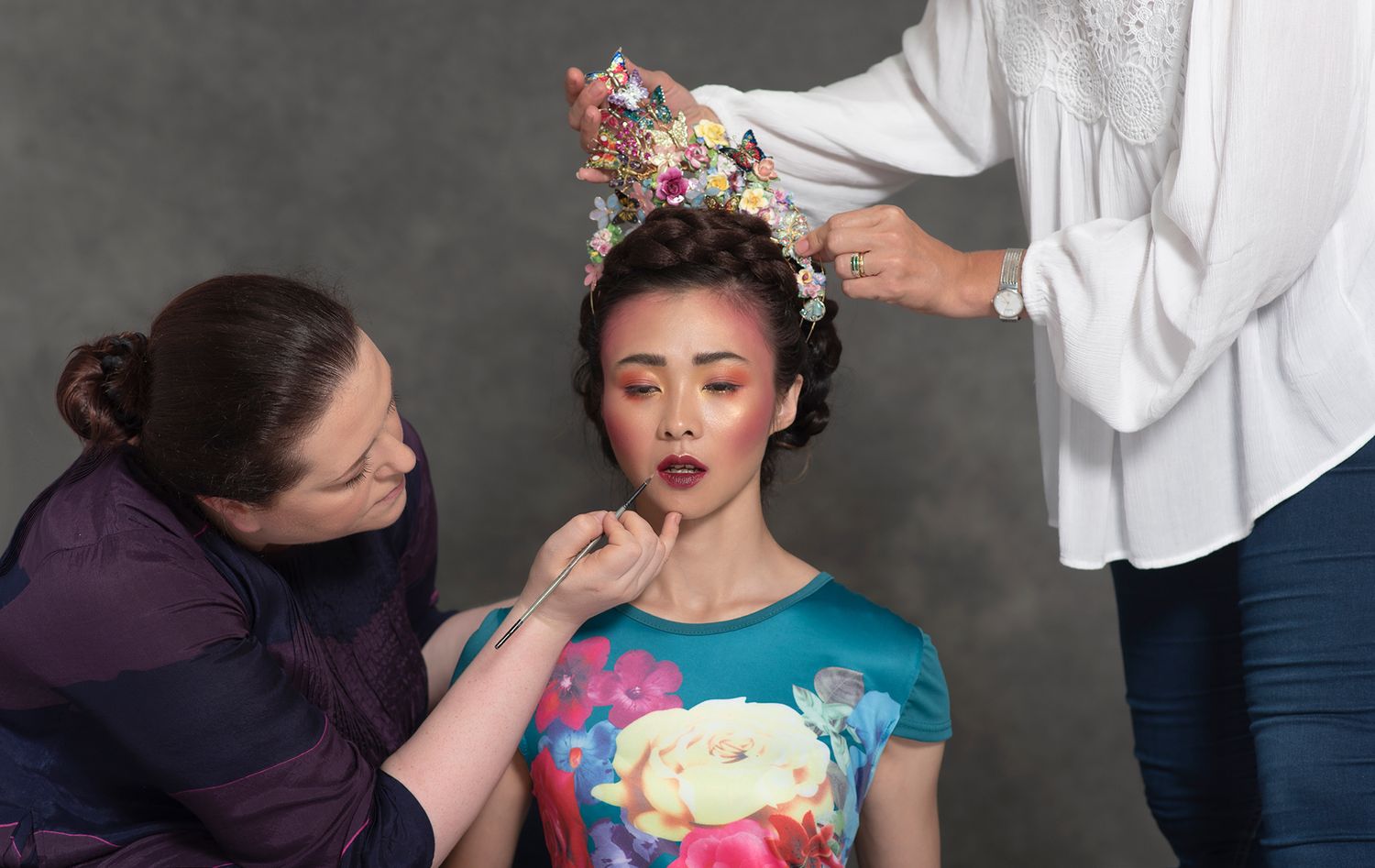 Behind the scenes of a fashion photoshoot with stylists preparing a model.