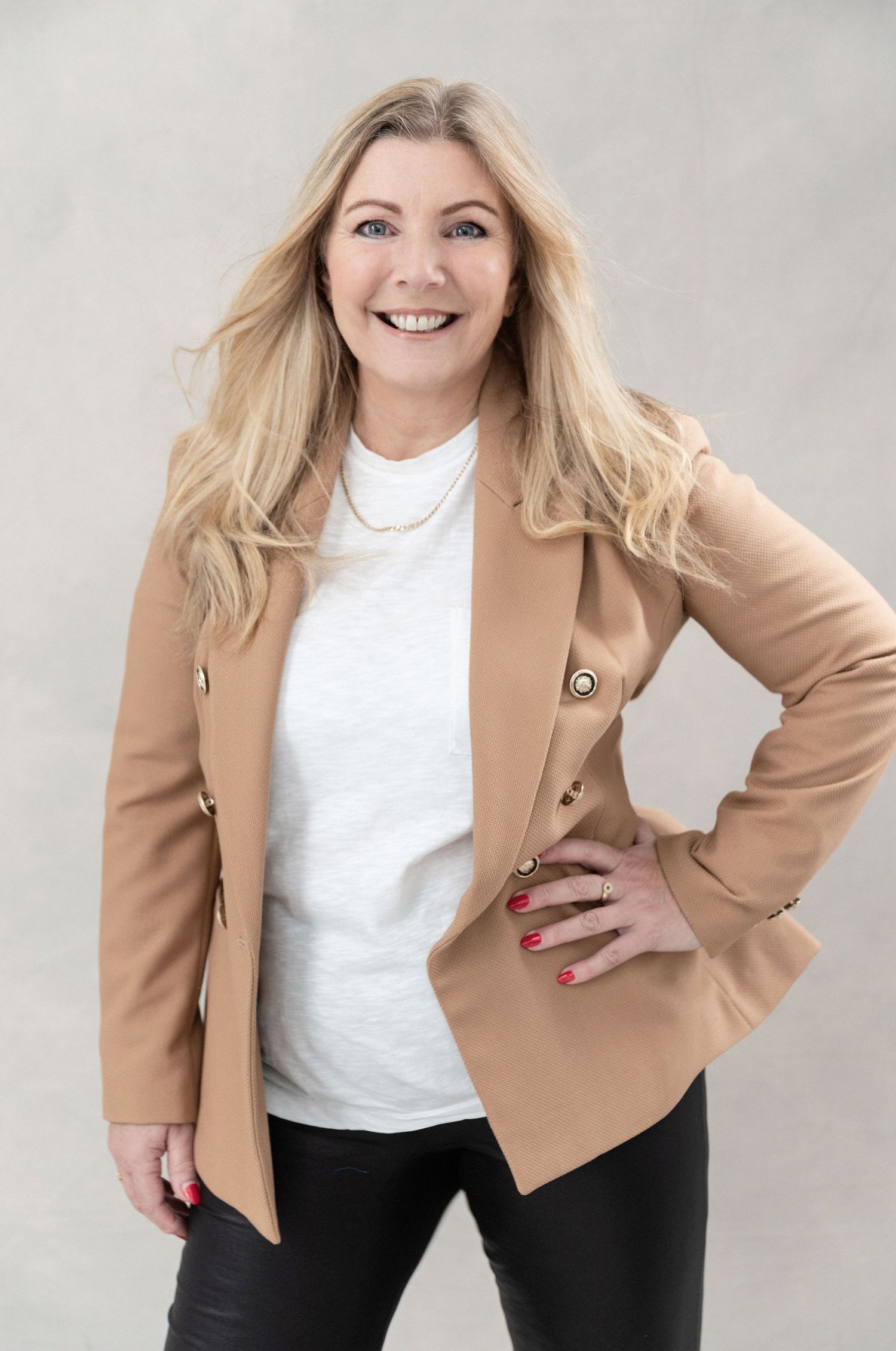 Professional portrait of someone in a tan blazer and white top posing confidently.