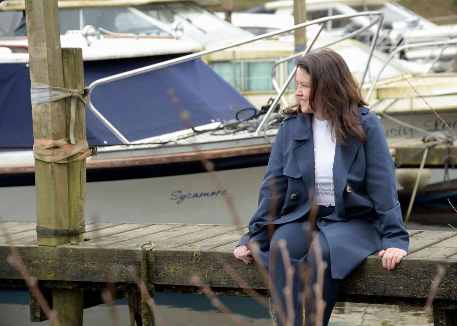 Woman in denim sitting on wooden dock by boats at a marina on a sunny day.