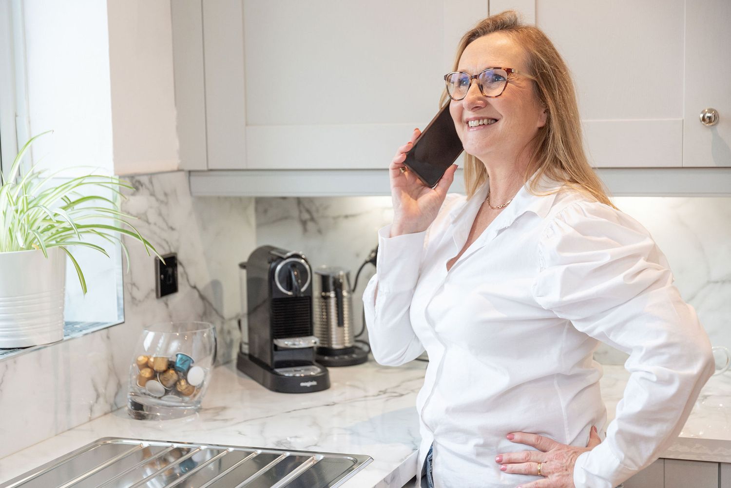 Person in white shirt talking on phone in modern kitchen with marble backsplash.