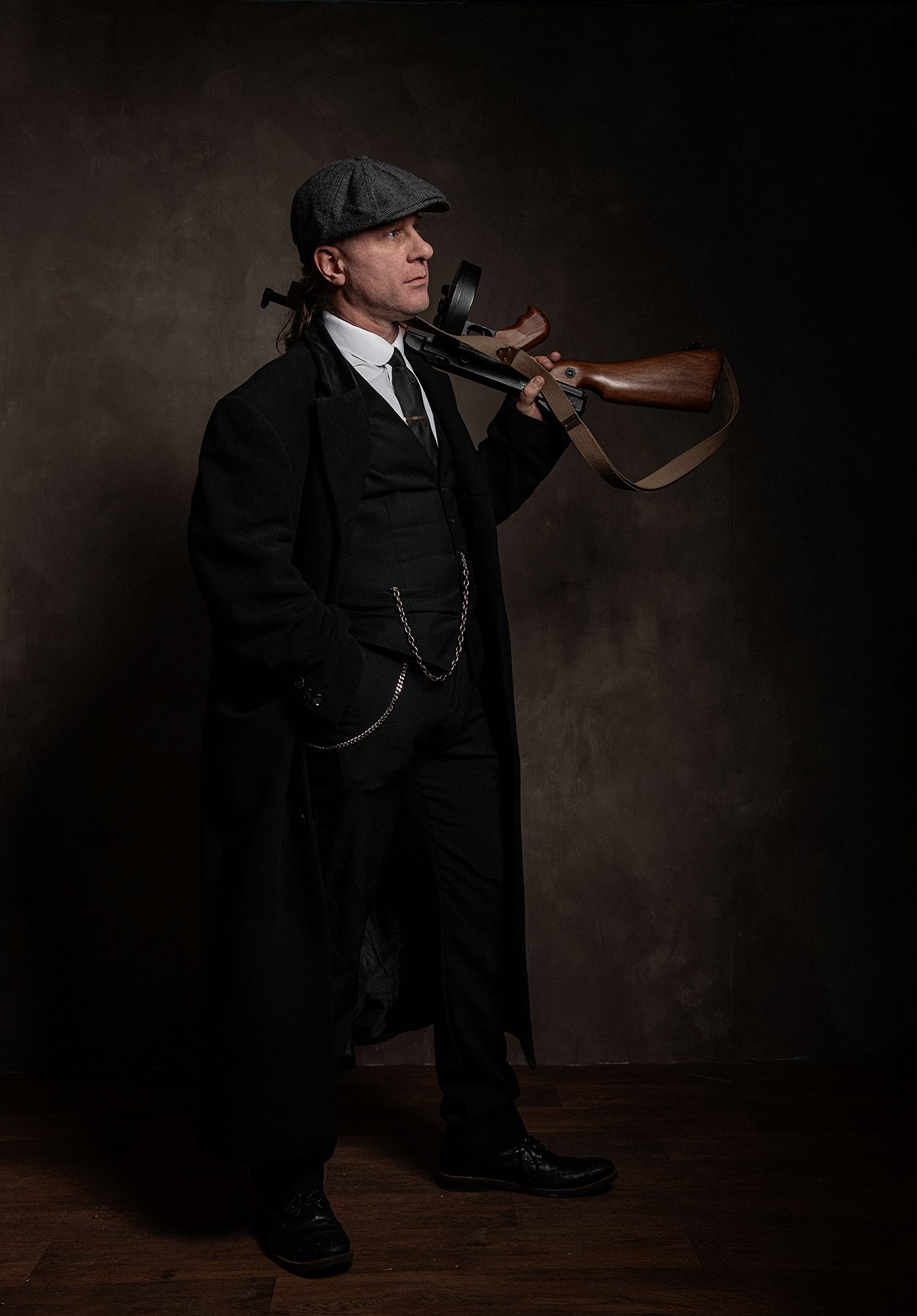 Figure in black period costume and flat cap holding vintage rifle.