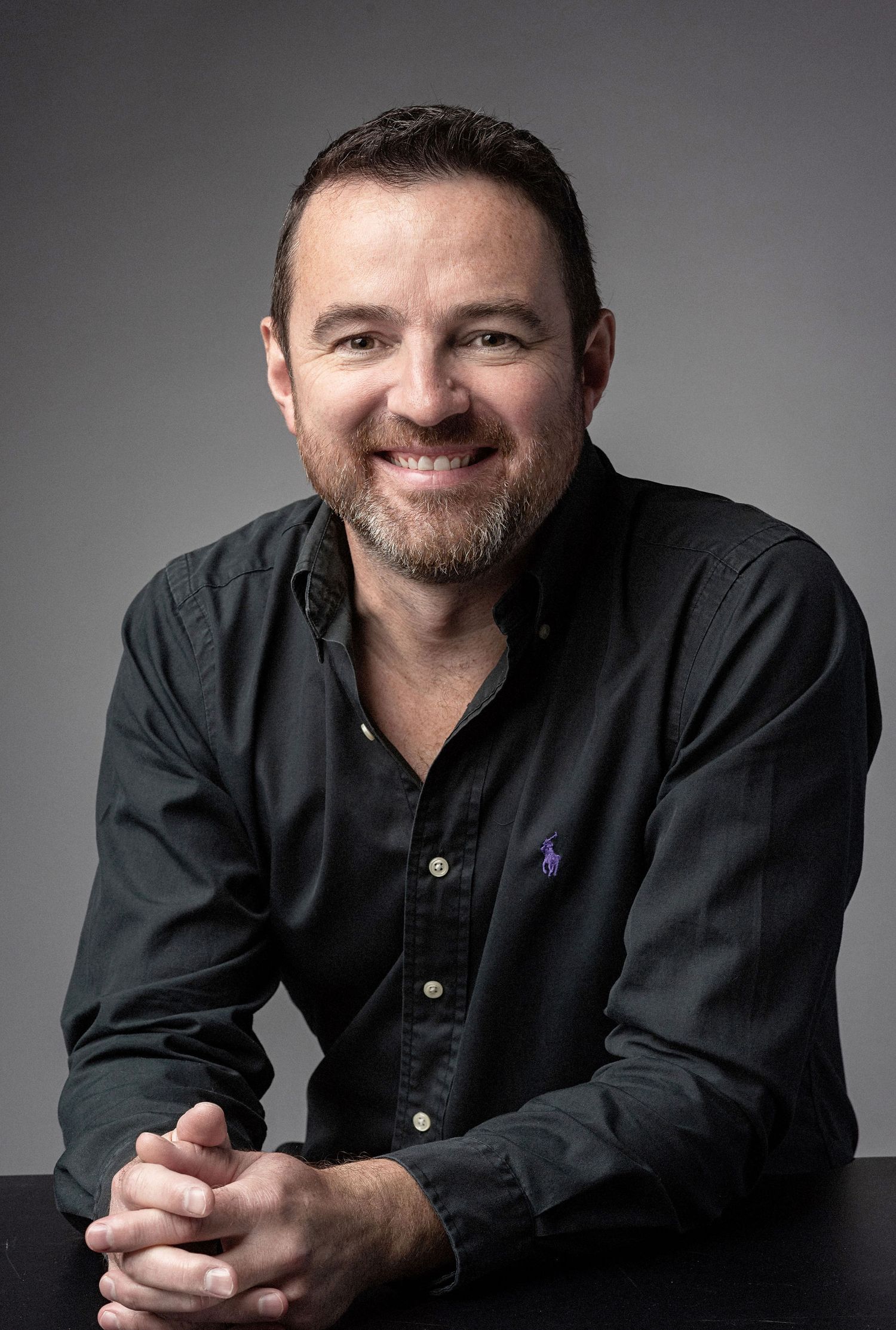 Professional headshot of a person in dark shirt smiling against grey background.