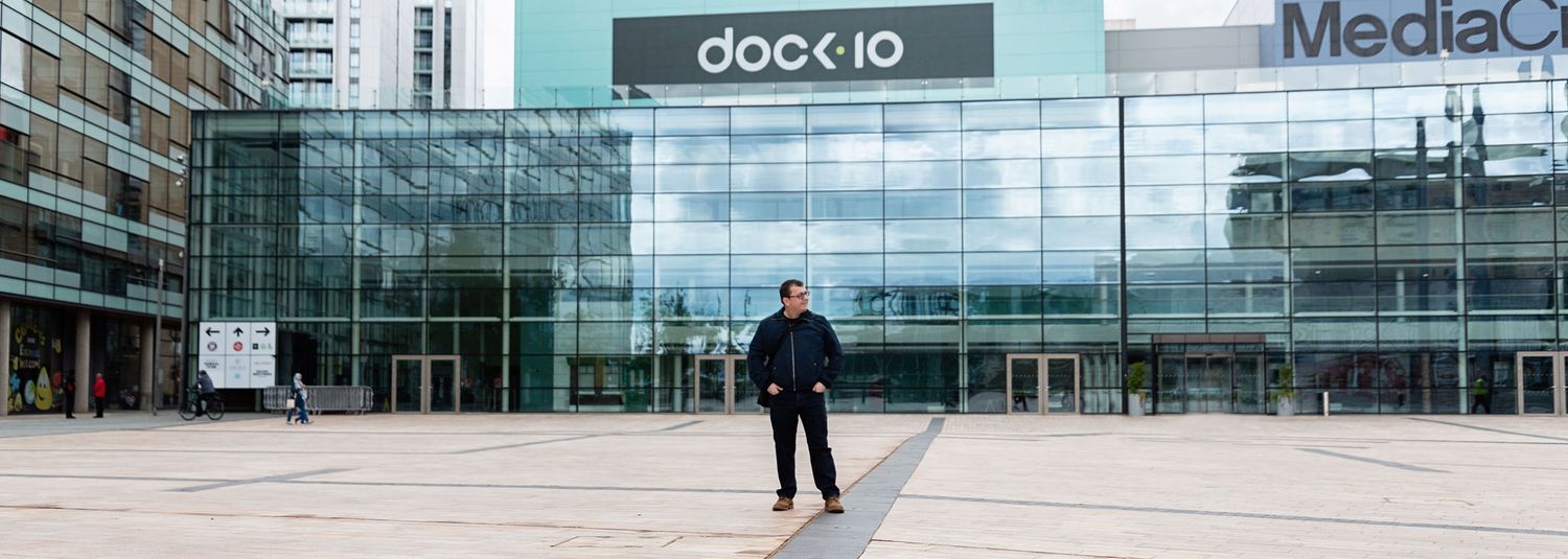 Person standing in front of modern glass building entrance with dock.io signage.