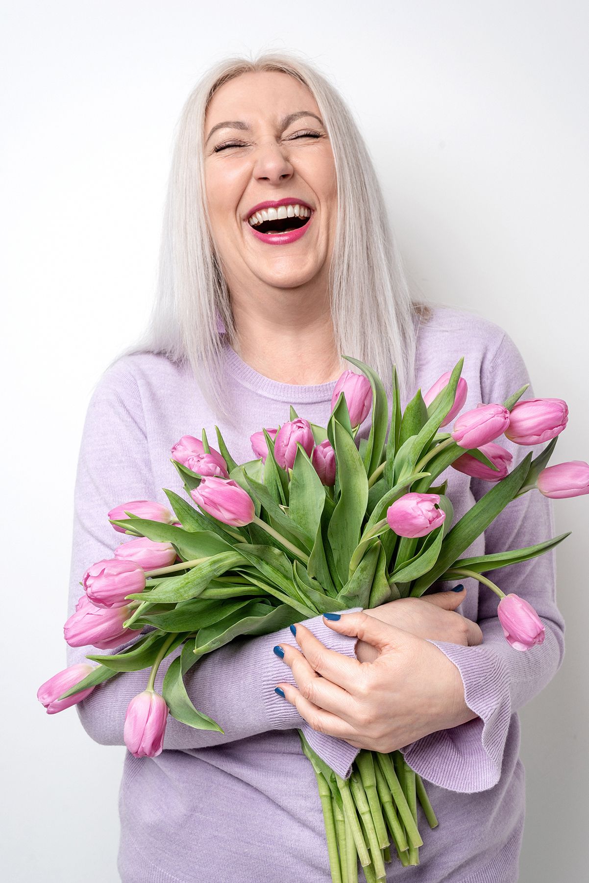 A joyful series showing someone in a lilac sweater holding pink tulips against a white background.