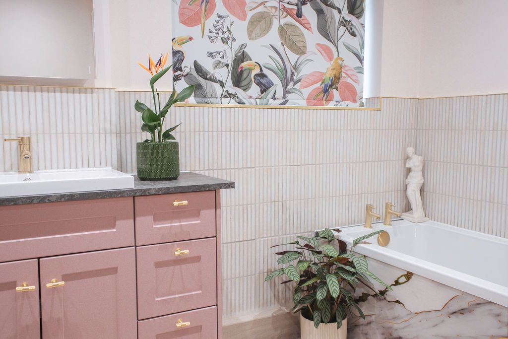 Modern pink bathroom interior with floral wallpaper, white cabinets, and indoor plants creating a spa-like atmosphere.