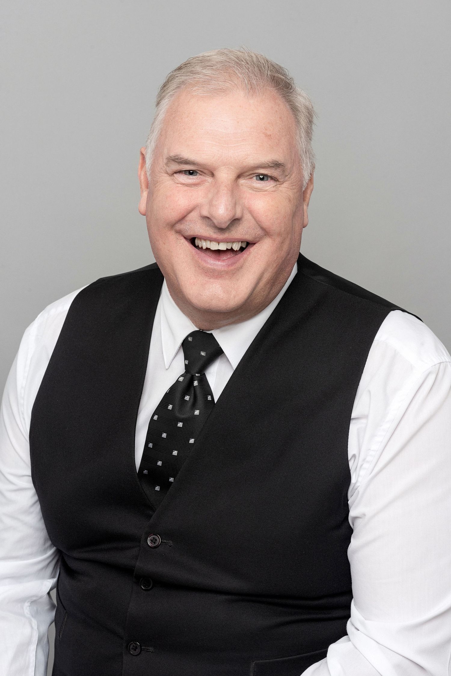 Professional headshot of someone in a black vest and polka dot tie smiling at the camera.