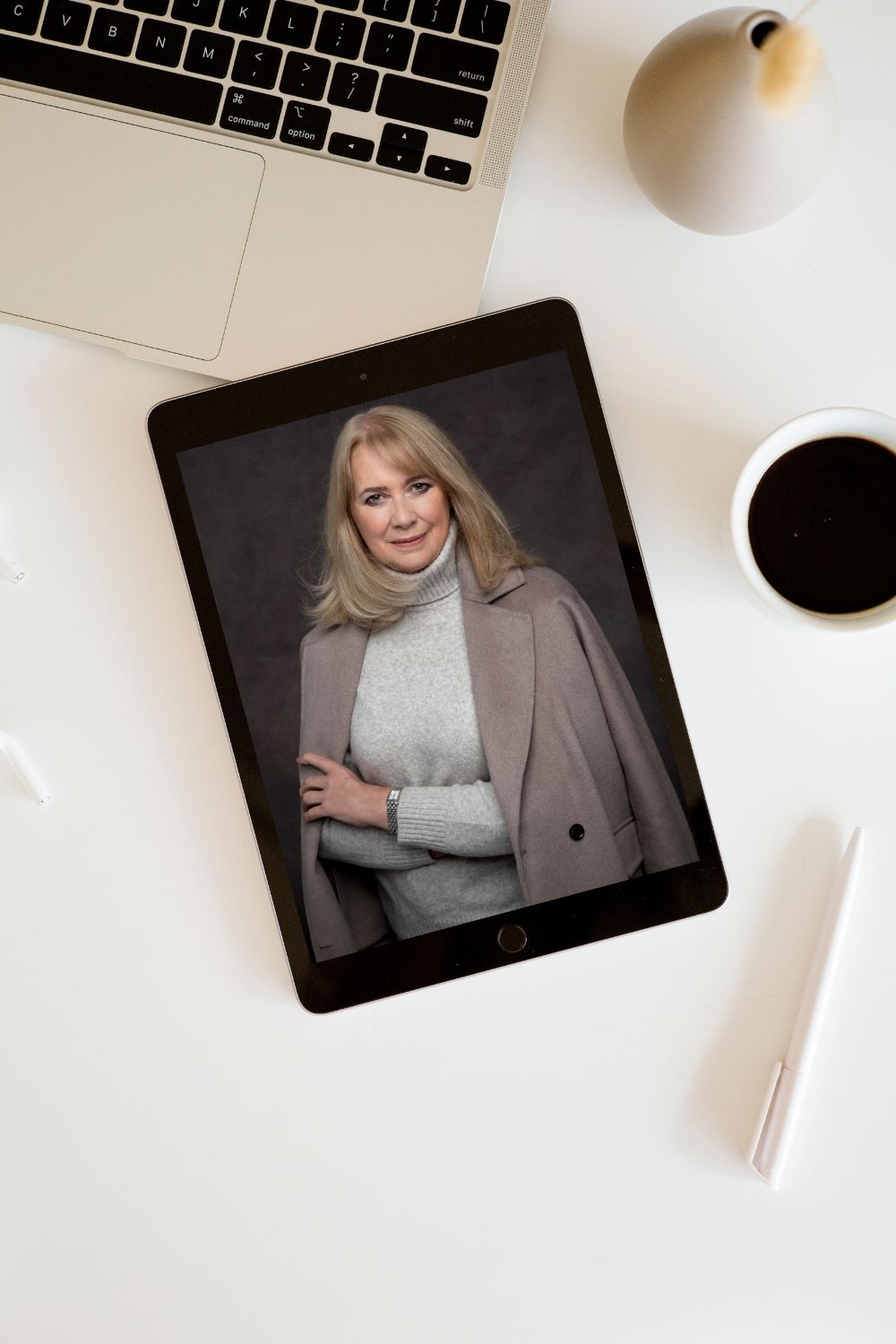 Workspace setup with laptop, tablet displaying portrait, coffee cup and desk accessories on white surface.