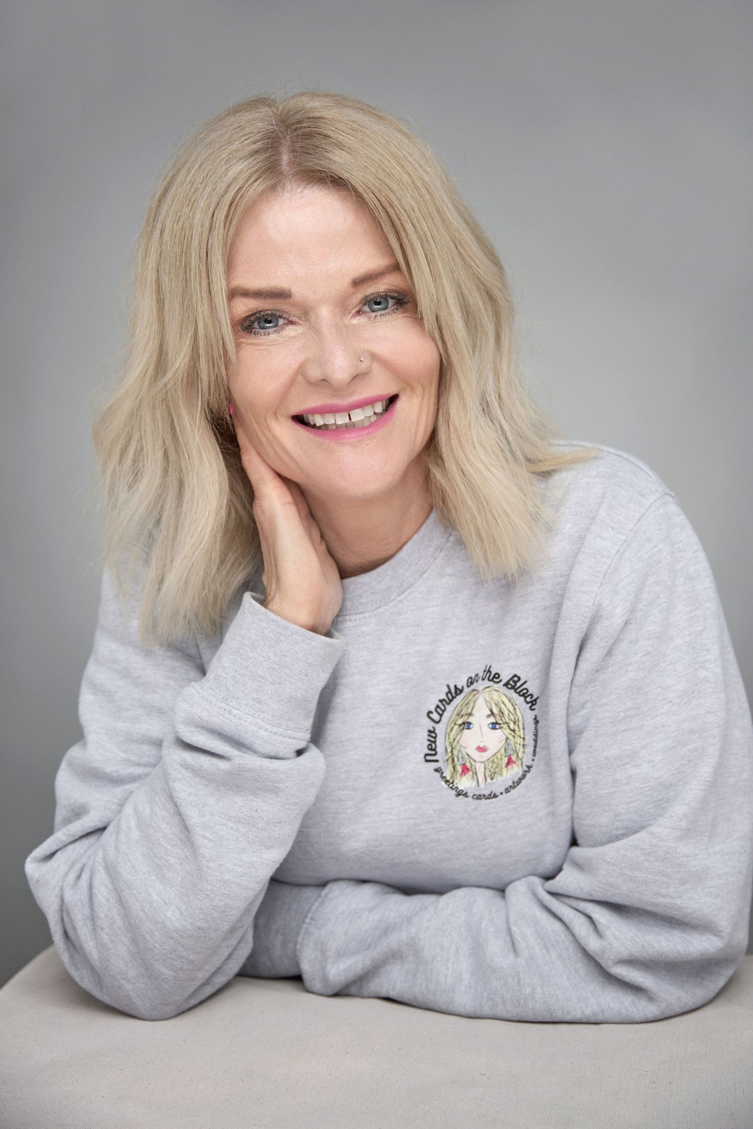 Portrait of person in gray sweatshirt with embroidered anime design resting hand on neck.