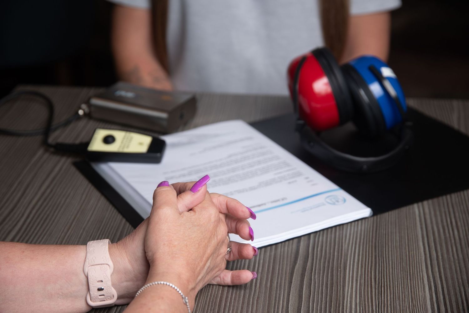 Close-up of hands writing on documents with red and blue hearing protection equipment visible.