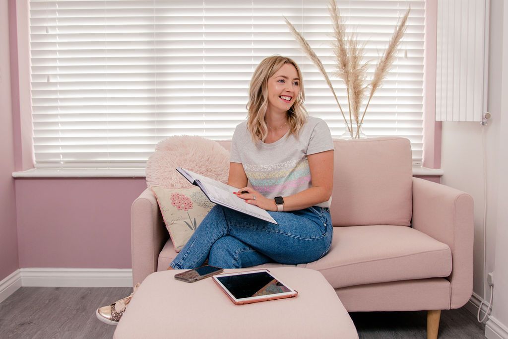 Person lounging on pink couch with tablet and stylus while working from home in cozy living room.