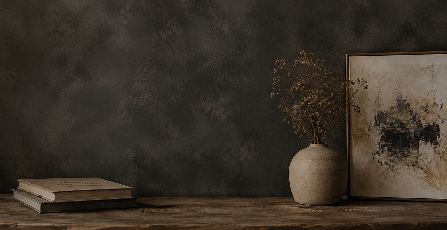 A rustic wooden shelf with stacked books, a ceramic vase with dried flowers, and a framed abstract artwork against a dark wall.