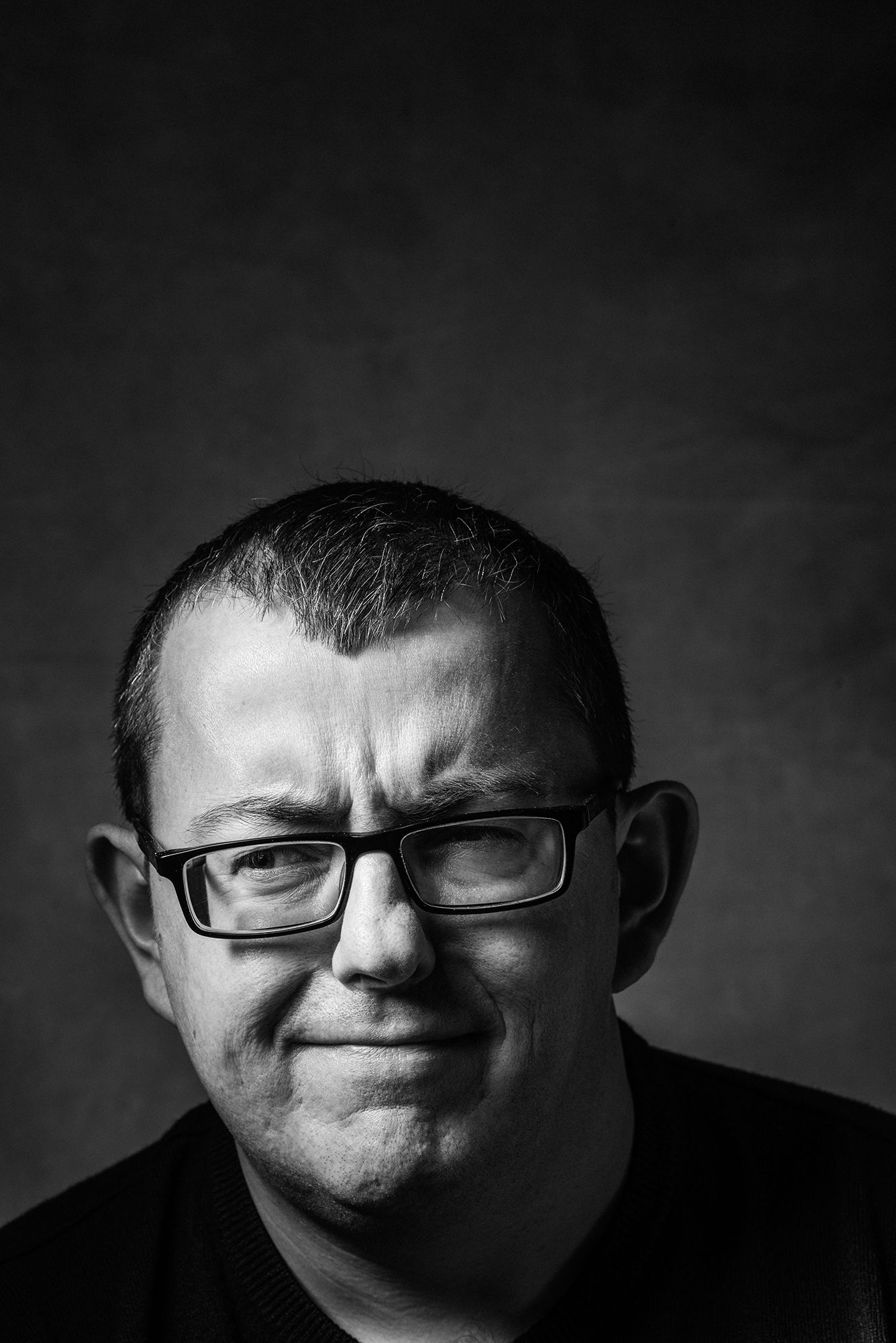 Black and white portrait of someone wearing glasses and a black shirt against a dark background.