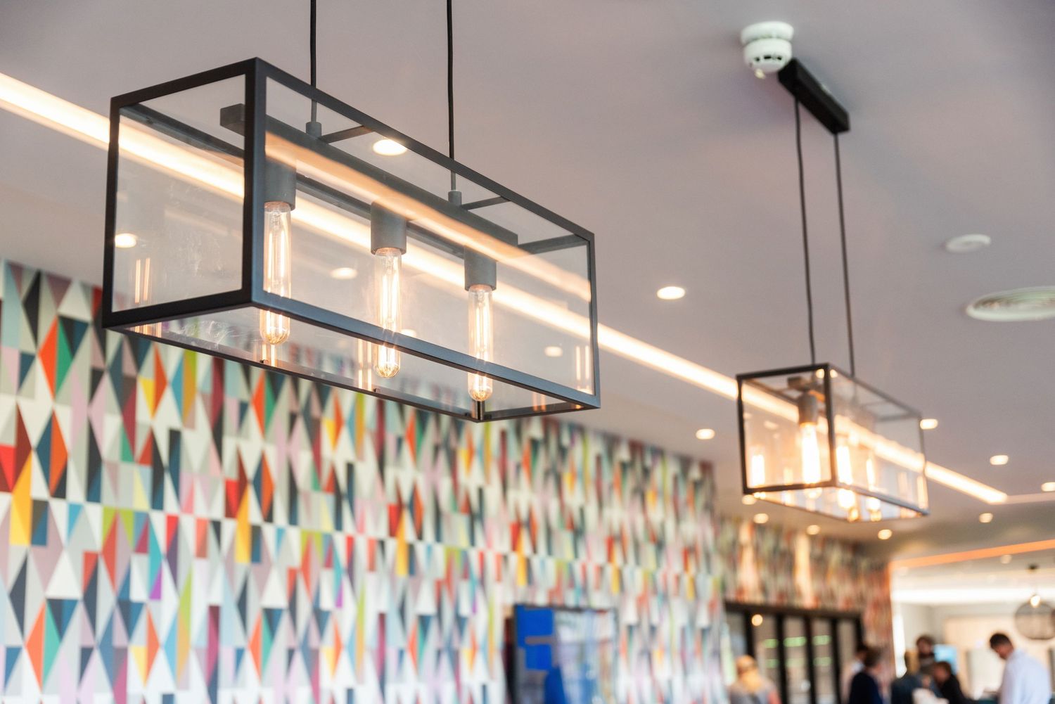 Modern rectangular pendant lights hanging over geometric patterned wall in hotel lobby.