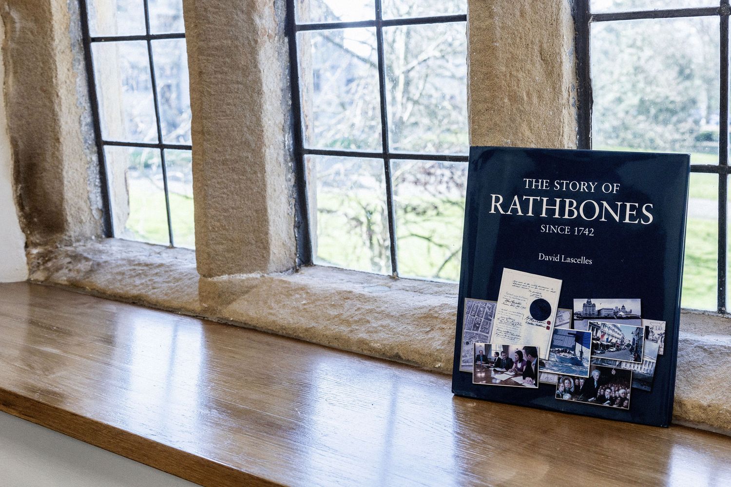 Book titled 'The Story of Rathbones' displayed on a stone windowsill with leaded windows.