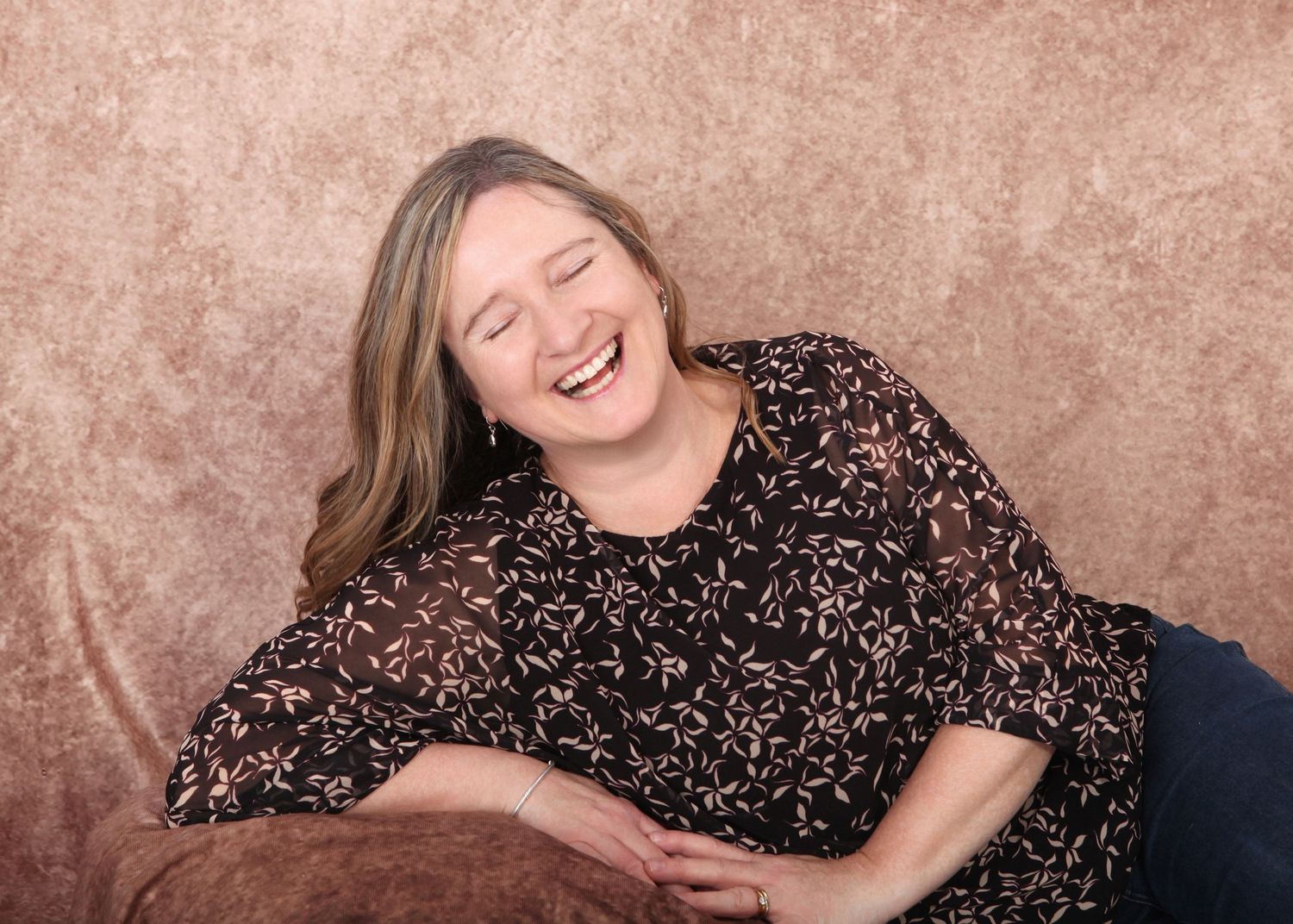 A person in a floral print dress reclines comfortably against a brown textured backdrop during a portrait session.