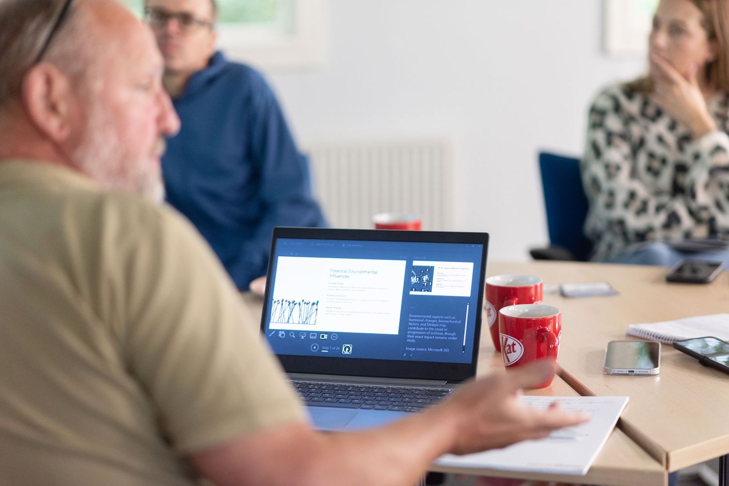 People sitting at tables with laptops and coffee cups during a professional business meeting or training session.