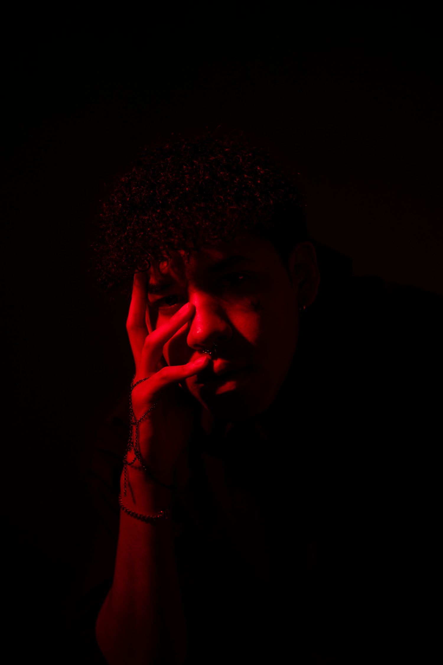 Artistic portrait bathed in red light with dramatic hand gesture.