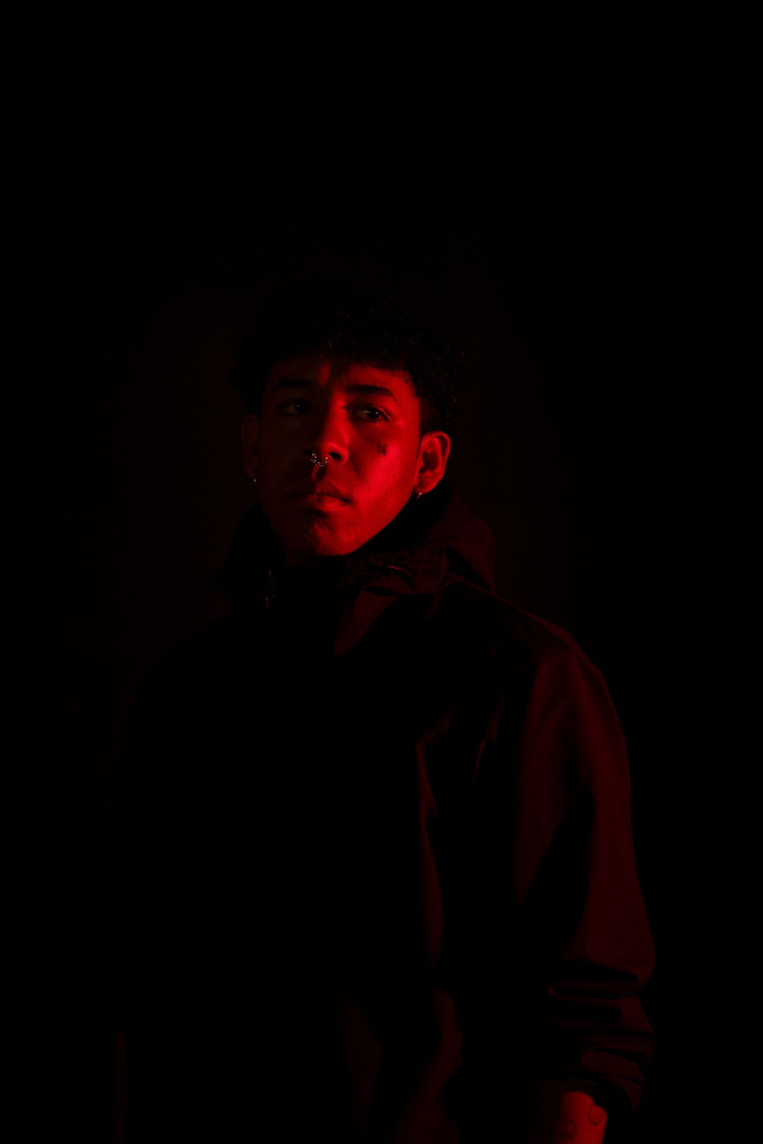 Mysterious portrait bathed in deep red lighting shows a shadowy figure emerging from darkness.