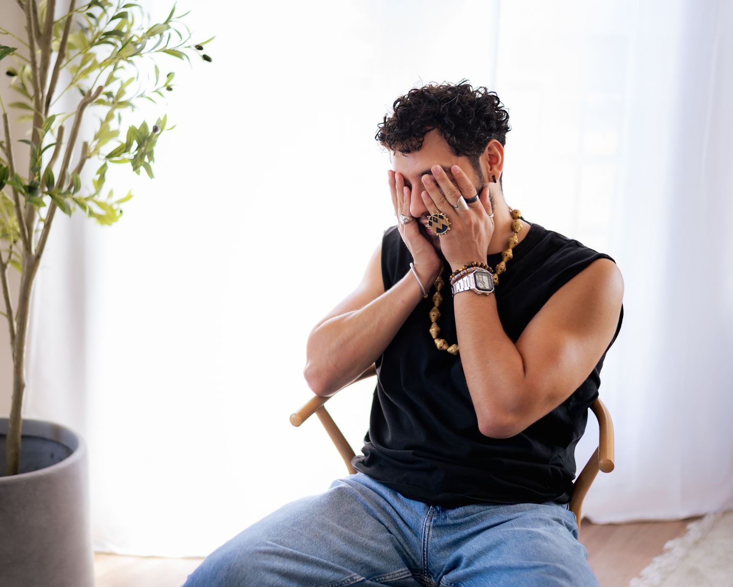 Person sitting in chair covering face with hands in emotional distress against white background.