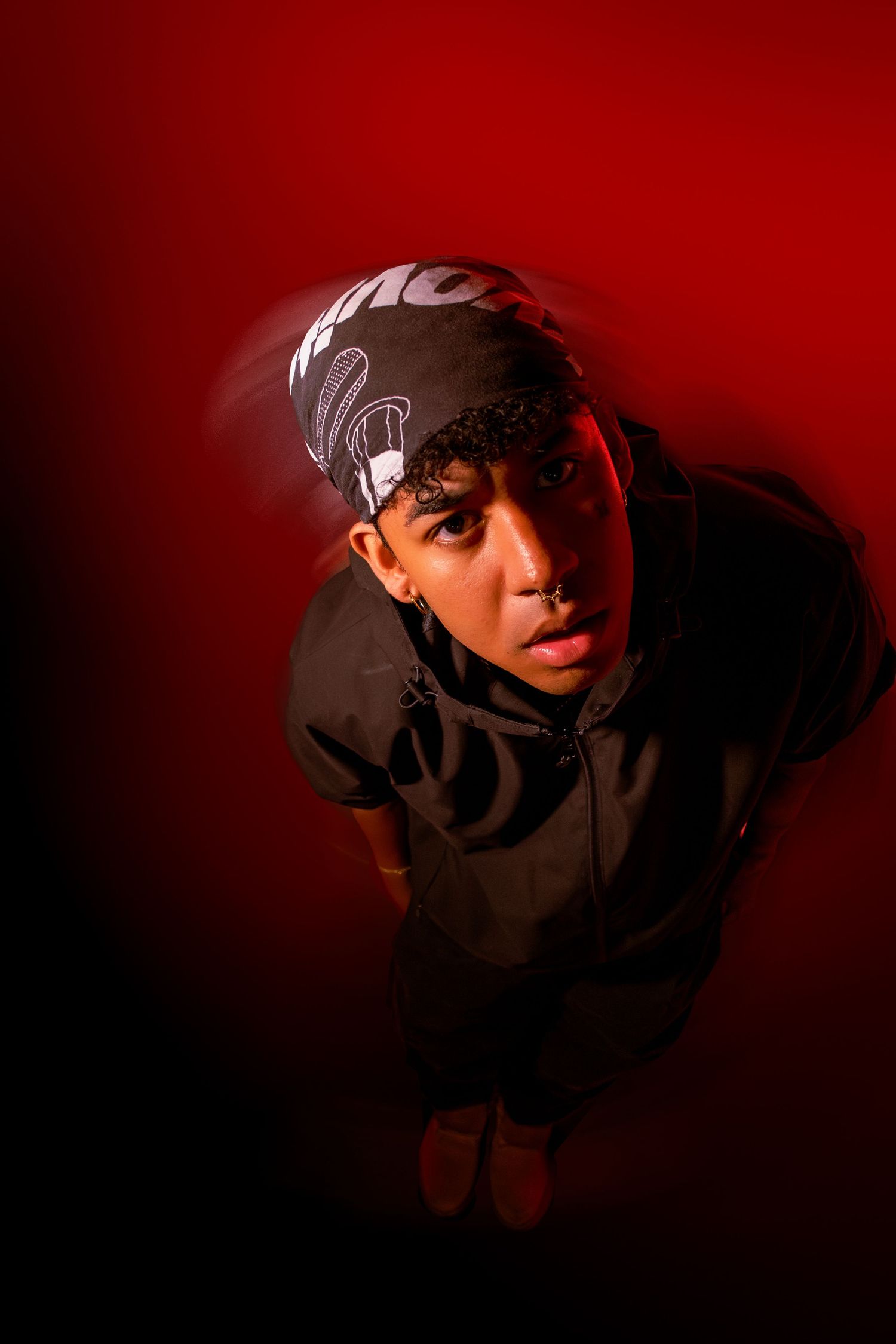 Dramatic portrait series against deep red background showing figure in baseball cap with moody lighting and shadows.