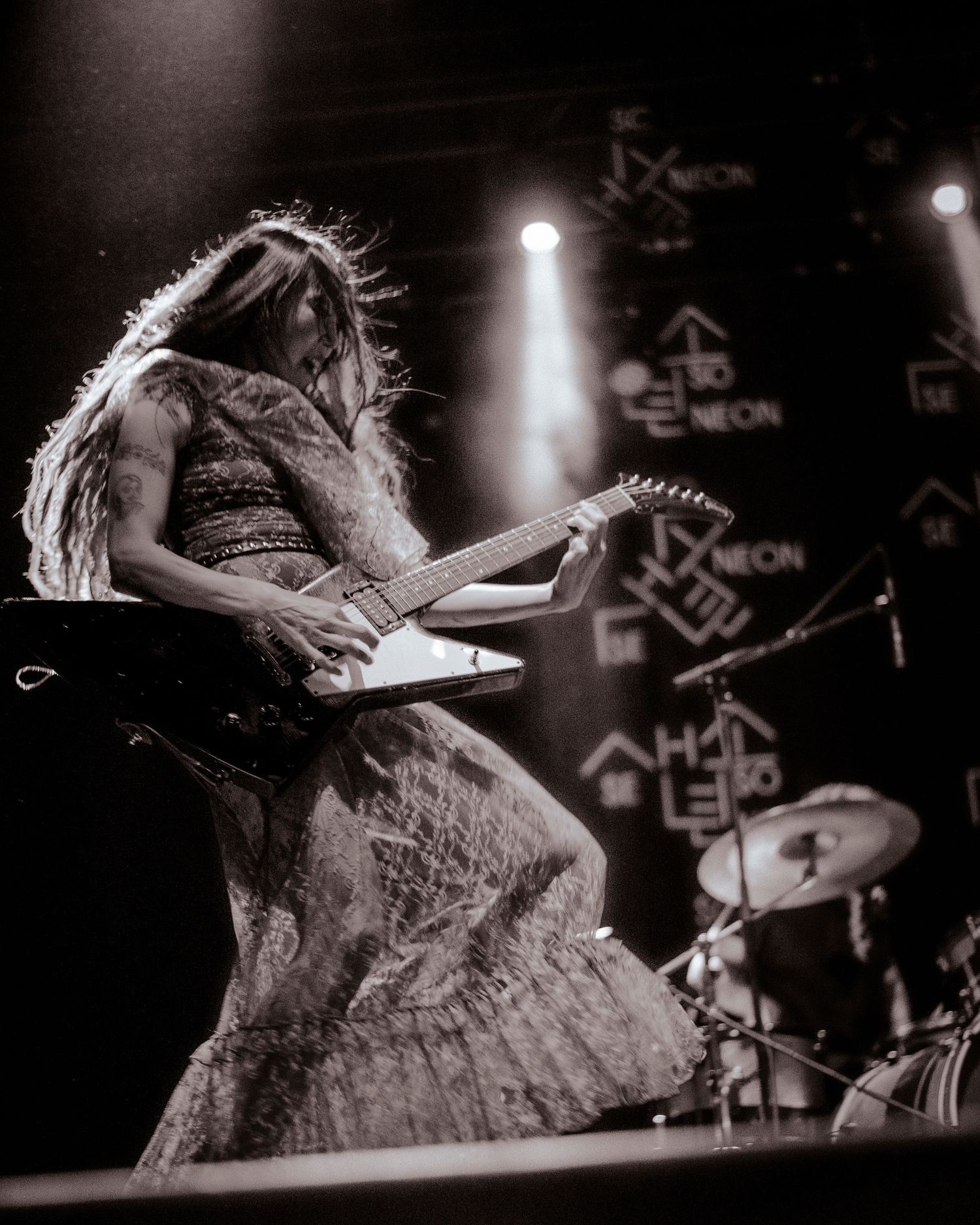 Black and white concert photo of performer with flowing hair playing guitar on stage.